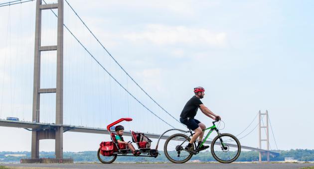 A man cycling in front of a bridge, towing a toddler carriage with his bike.