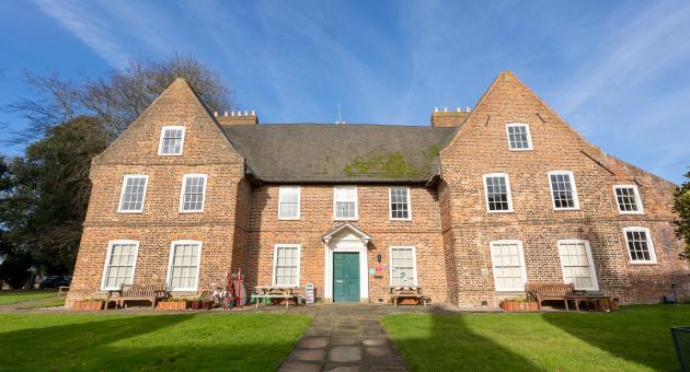 A thatched manor house with gardens and gates from the front