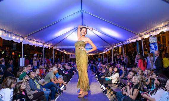Model Wearing a Gold Dress Strikes a Pose at End of Runway as Guests Watch from Seats