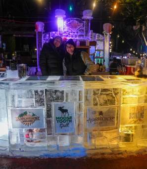 Two bartenders serving drinks behind an illuminated ice bar at Funky Ice Fest at Adirondack Pub & Brewery in Lake George Village