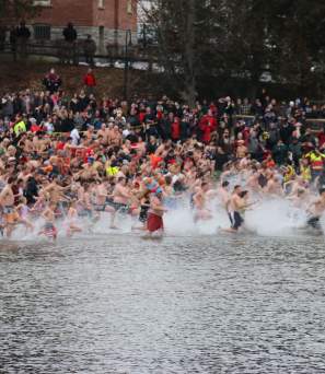 A crowd of swimmers running toward Lake George in winter for the polar plunge event.