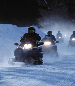 A group of snowmobile riders traveling down a snowy road.