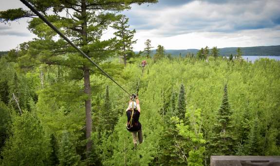 Female ziplining through the woods with lake views
