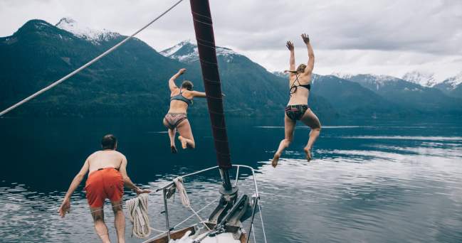 Three people in swimsuits jumping off a boat into the water below.