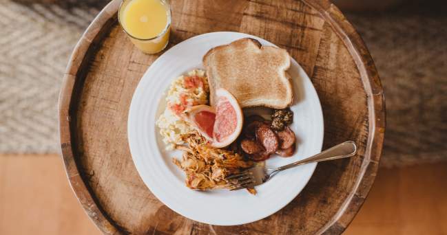 A glass of orange juice sits next to a plate of eggs, toast, grapefruit, and sausage.