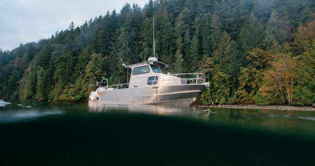 A fishing boat sits on the water with a view of the forest behind it.