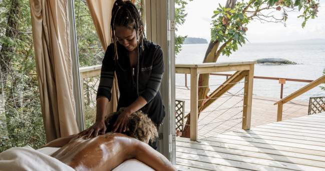 A woman enjoys a massage in a spa tent overlooking the ocean.