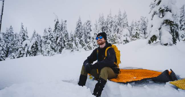 A man grins as he sits down to take a rest from snowshoeing.