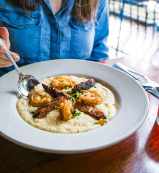 Woman sitting in front of a bowl of shrimp and grits at Uptown