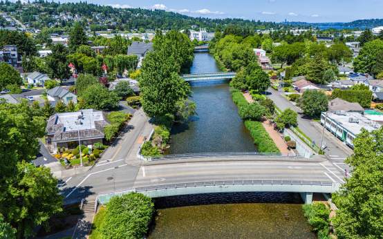Aerial view of the Cedar River Trail in Renton, featuring the Cedar River flowing beneath a bridge, tree-lined pathways, surrounding neighborhoods, and scenic urban green space.