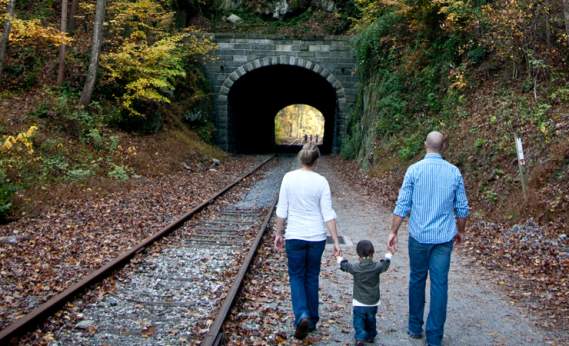 A small child holds hands with their parents as they walk along the rail trail toward Howard Tunnel in fall
