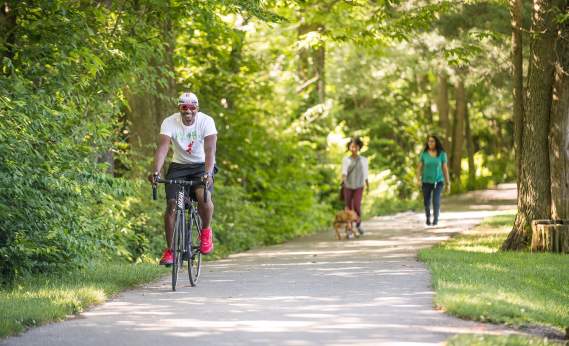Man riding bike and women walking along wooded rail trail