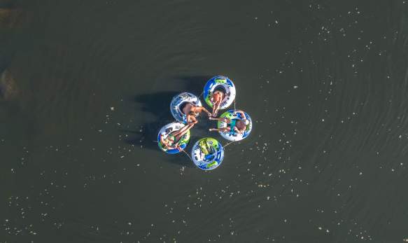 The overview of five tubes with adults sitting in them on a lake