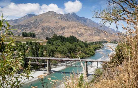 Tall trail bridge over blue river stream with mountains in background