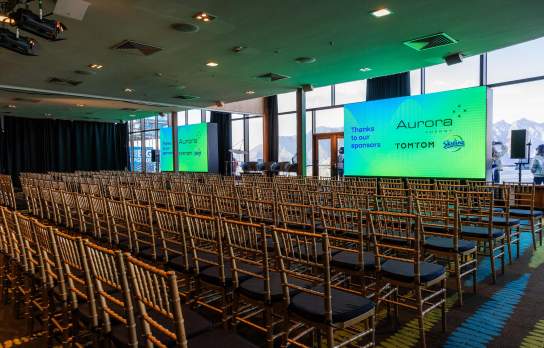 Two screens, a stage and chairs setup for a speaker session at a conference at Skyline, Queenstown