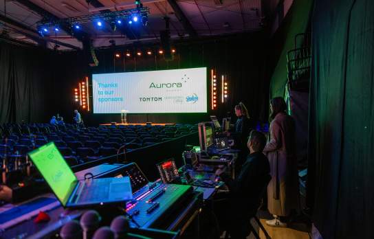 Behind the scenes of an event tech setup with large screens, lights and computer controls