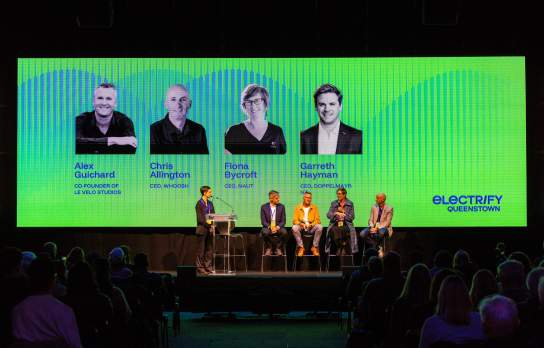 A dark event with a panelist on stage in front of a big screen