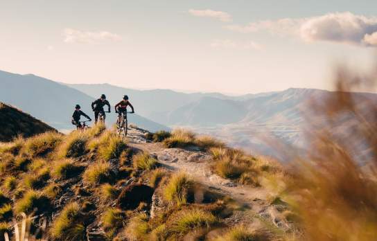 Three mountain bikers on top of mountain with mountain range in background
