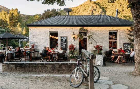 Old white cottage-looking pub with people sitting al fresco and green mountains in the background