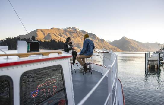 A couple sitting on the front of Perky's Floating Bar in Winter with lake and mountain views