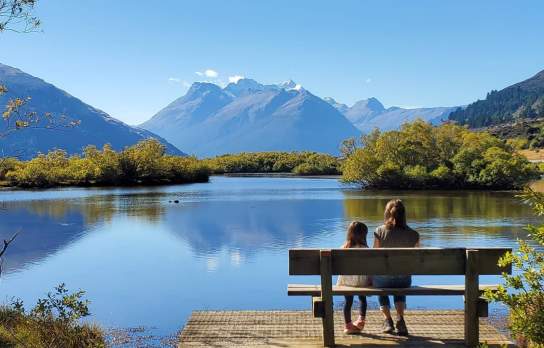 Mum and daughter sitting by lake with view of mountains in the background