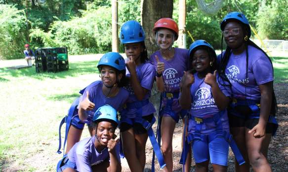 A group of girls pose for a photo while wearing helmets at the Challenge Course.