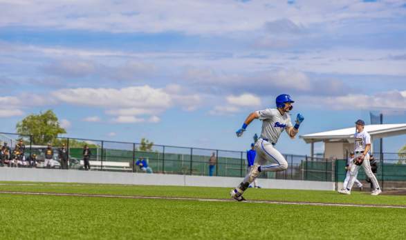 Baseball player running with another baseball player in the background.