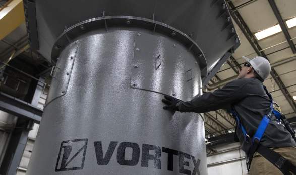 A worker inside a shop touching a piece of equipment with the name "Vortex" on it.