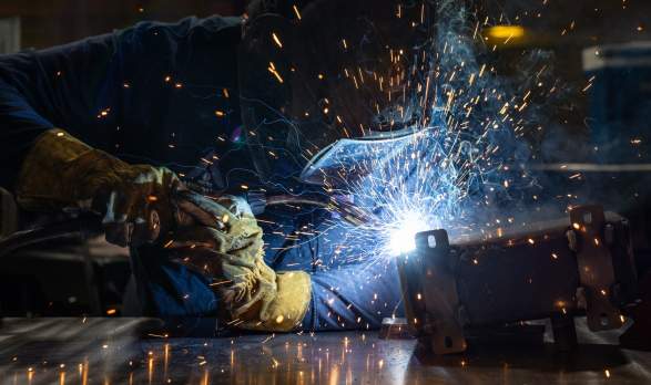 A worker in PPE welding in a shop.
