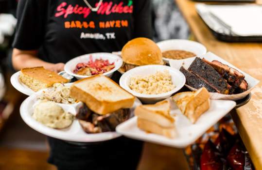 multiple different dishes of texan barbeque being served by a waitress