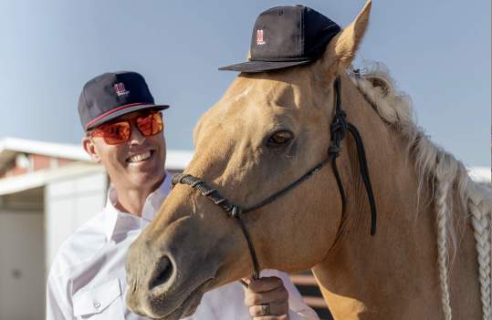 Man in an Amarillo Boot Hat standing with his horse in an Amarillo Boot Hat on it