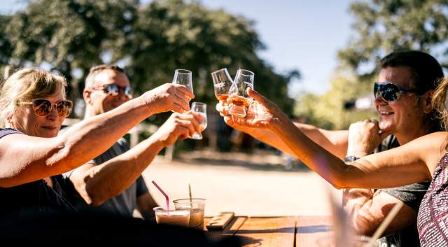 Four people sitting outside on a patio holding up small tasting glasses with bourbon at Garrison Brothers Distillery.