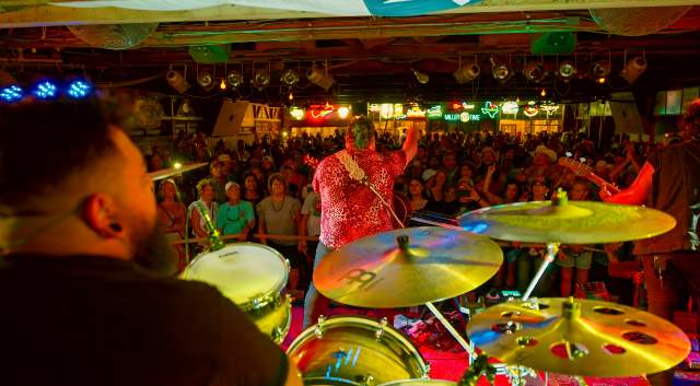 The band Kin Faux playing a show at Gruene Hall with people standing in the crowd in the background.