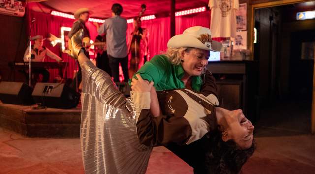 Two women in Western attire country dancing in a dance hall.