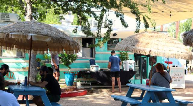 Veracruz All Natural food truck with people sitting at grass umbrella-shaded picnic tables.
