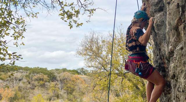 A woman in climbing harness climbing a rock wall at Reimers Ranch.