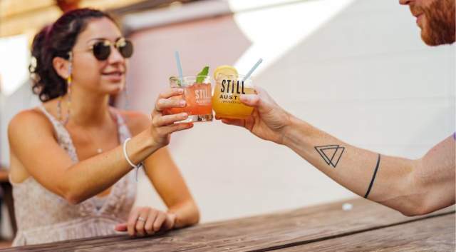 Image of a man and women holding their cocktails together on the patio at Still Austin Whiskey Co.