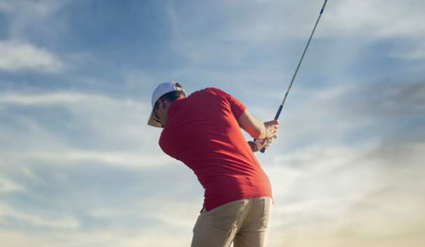 Golfer in red shirt, in middle of back swing at sunset.