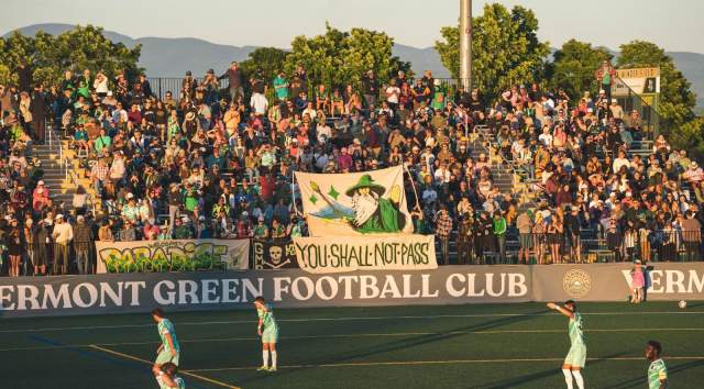 Vermont Green FC players on Virtue Field at sunset with the bleachers in the background.