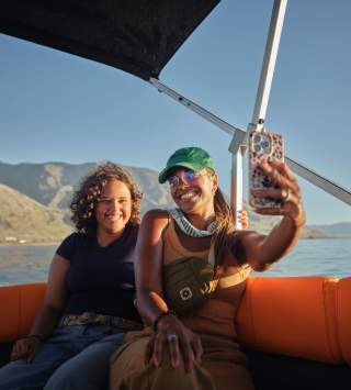 Two women on a pontoon boat taking a selfie with the great salt lake and antelope island in the background