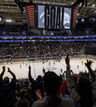 Hockey arena with fans cheering. scoreboard that reads GOAL, while players are on the ice sheet.