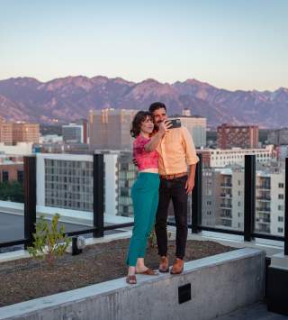 Couple standing and taking a selfie on the roof at Van Ryder with Salt Lake City Skyline and wasatch mountains in the background