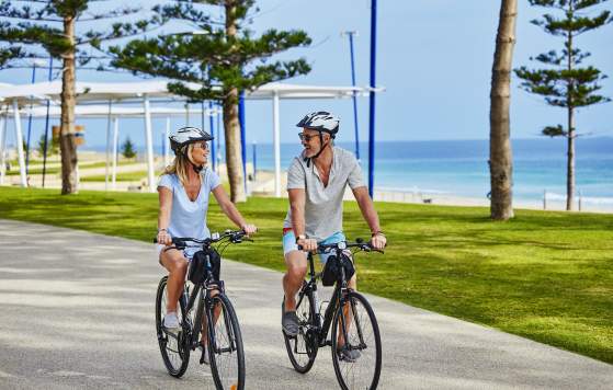 Couple cycling past Scarborough Beach, Sunset Coast