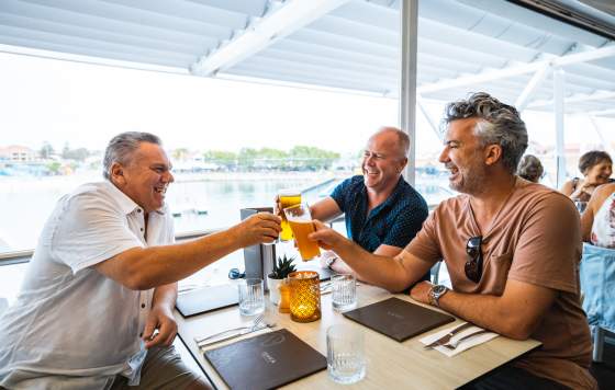 Three men toasting a drink together at a table overlooking the Hillarys Boat Harbour.