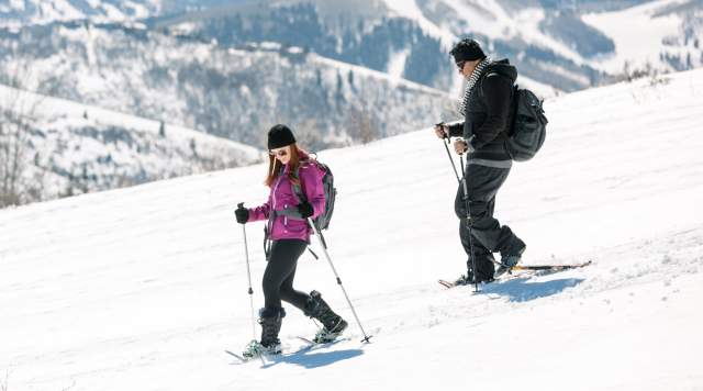 Couple snowshoeing down hill with ski resort in background