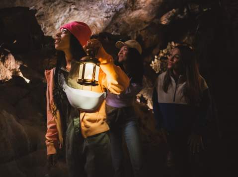Three women, one with a lamp, exploring a dark, underground cave
