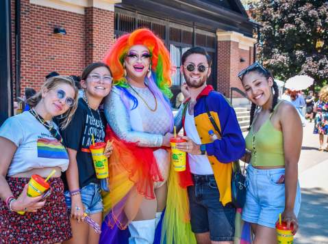 Four people posing with a drag queen at a street parade
