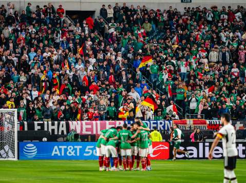 A huddle of soccer players in front of a goal in a crowd-filled stadium