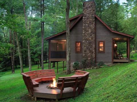 Exterior of a rustic, wood cabin with a fire pit outside and two red benches around it