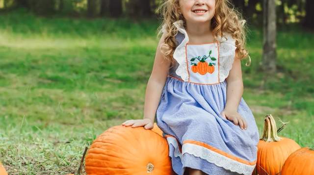 A young girl smiles at a pumpkin patch with multiple pumpkins.